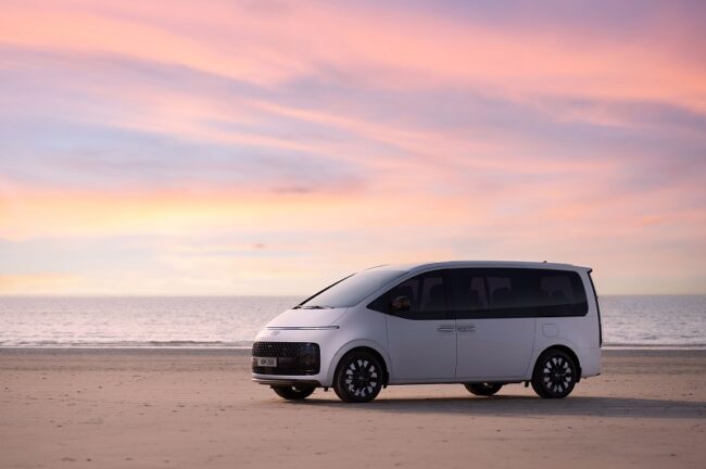 Silver passenger van parked on a beach at sunset, illustrating new vs. used van options in 2026.